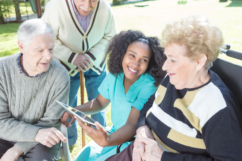 African nurse helping elderly people using tablet outdoor.